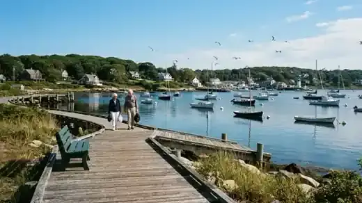 A quiet small-town harbor on the north shore of Long Island at morning with moored sailboats, a wooden boardwalk and an empty bench